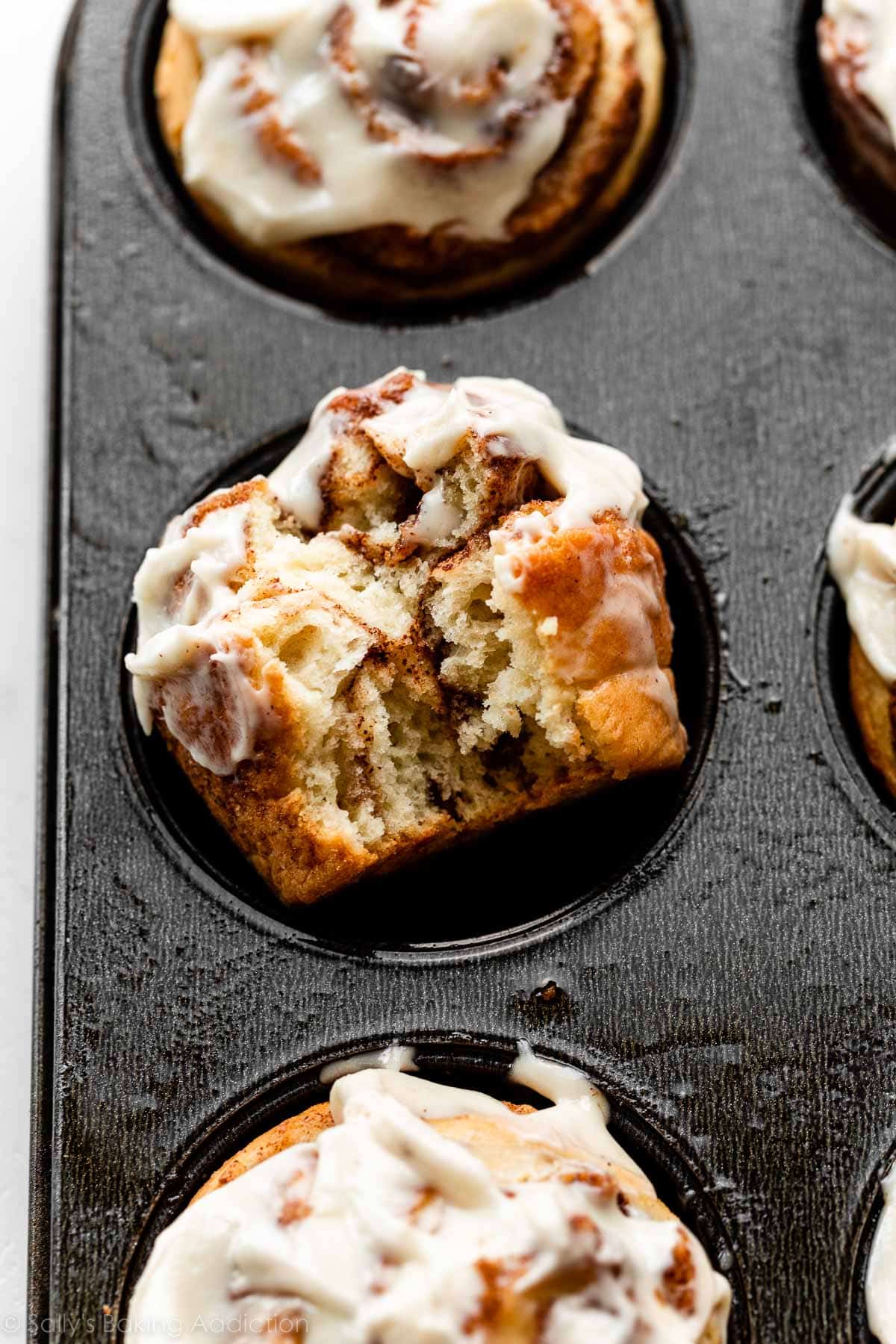 cinnamon roll muffin in muffin pan with bite taken out of it.