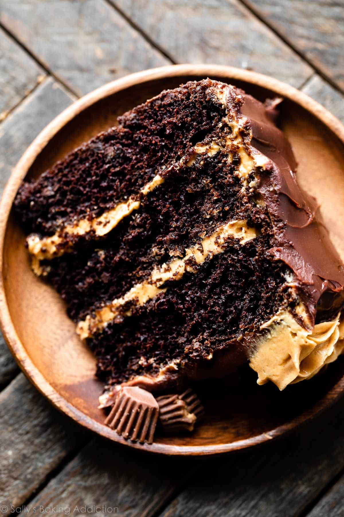 slice of 3 layer chocolate cake filled with peanut butter frosting on wooden plate.