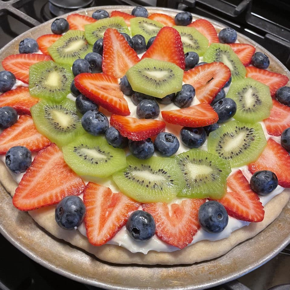 fruit pizza with strawberries, blueberries, and kiwi on top.