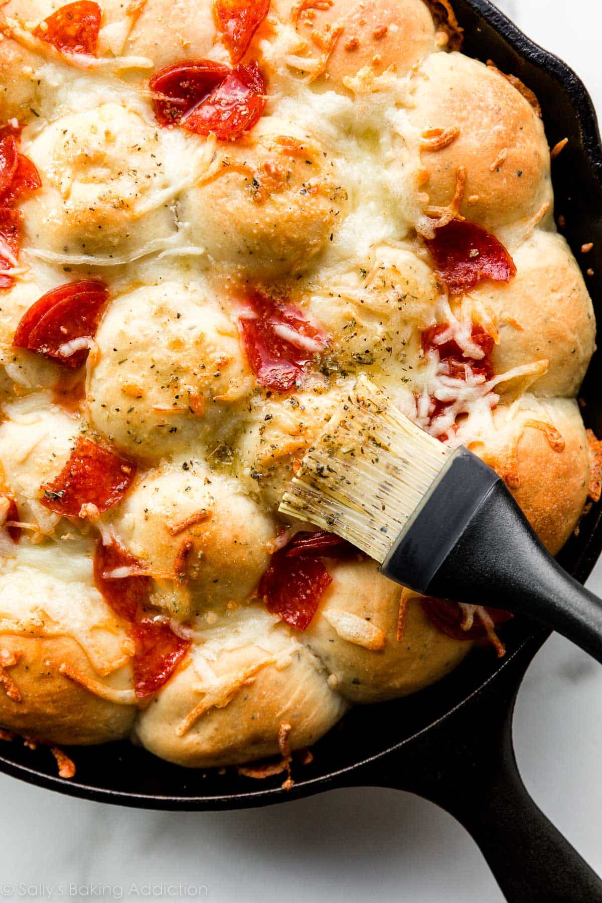 brushing garlic herb butter on pepperoni and cheese pizza topped pull apart rolls.