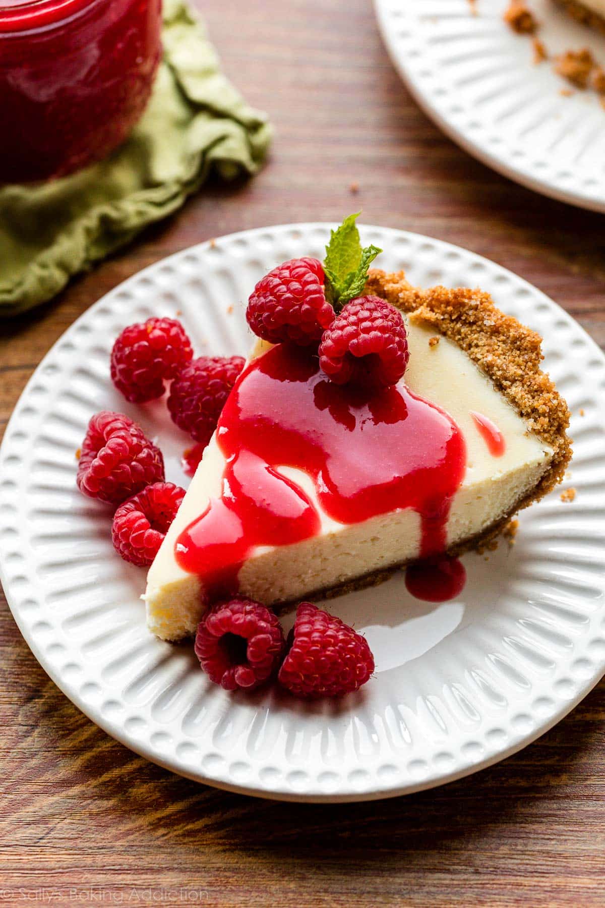 cheesecake pie slice on white plate with raspberry sauce and fresh raspberries on top.