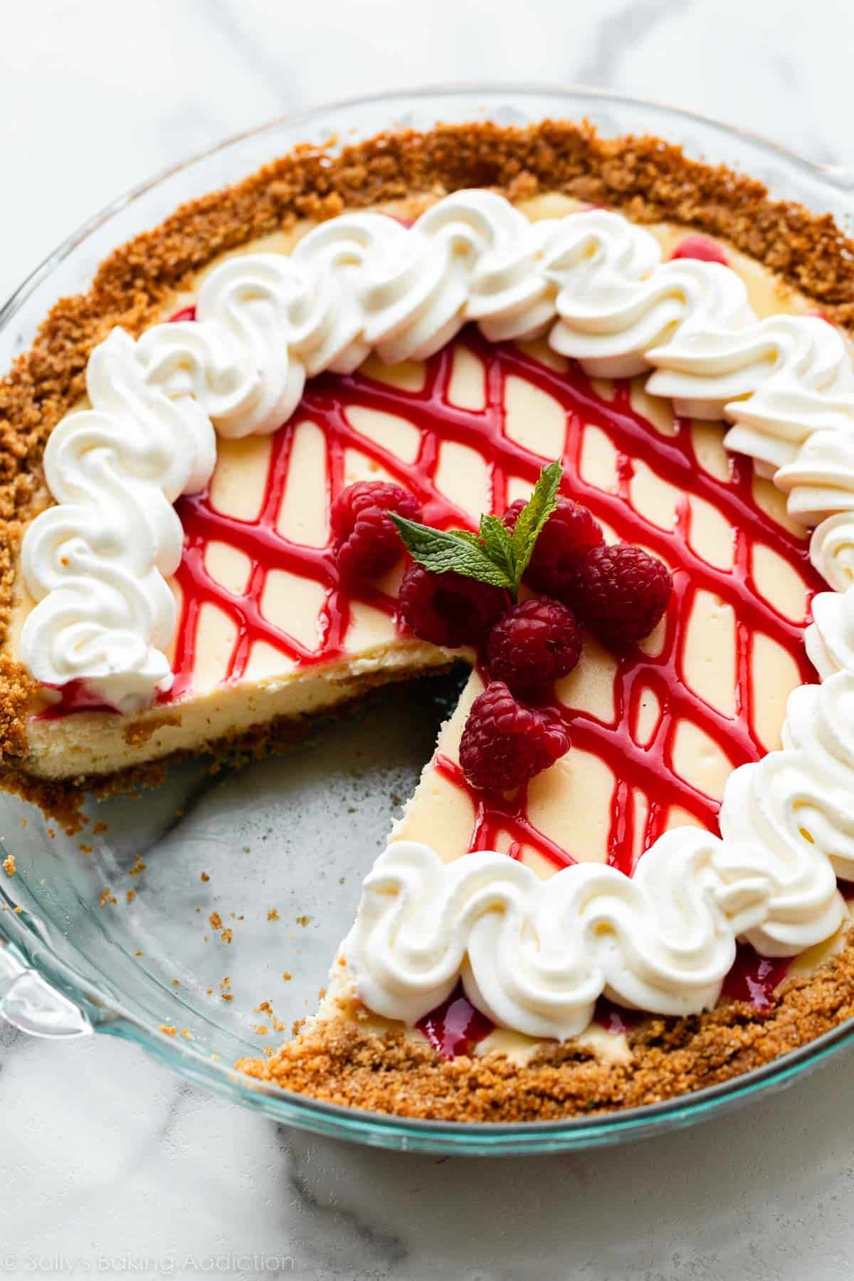 whipped cream and raspberry sauce topped cheesecake pie with 1 slice removed.