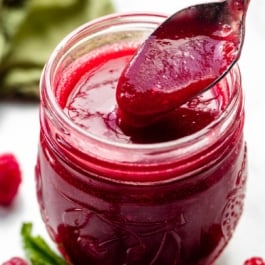 homemade raspberry dessert sauce in glass mason jar with spoonful being taken out.