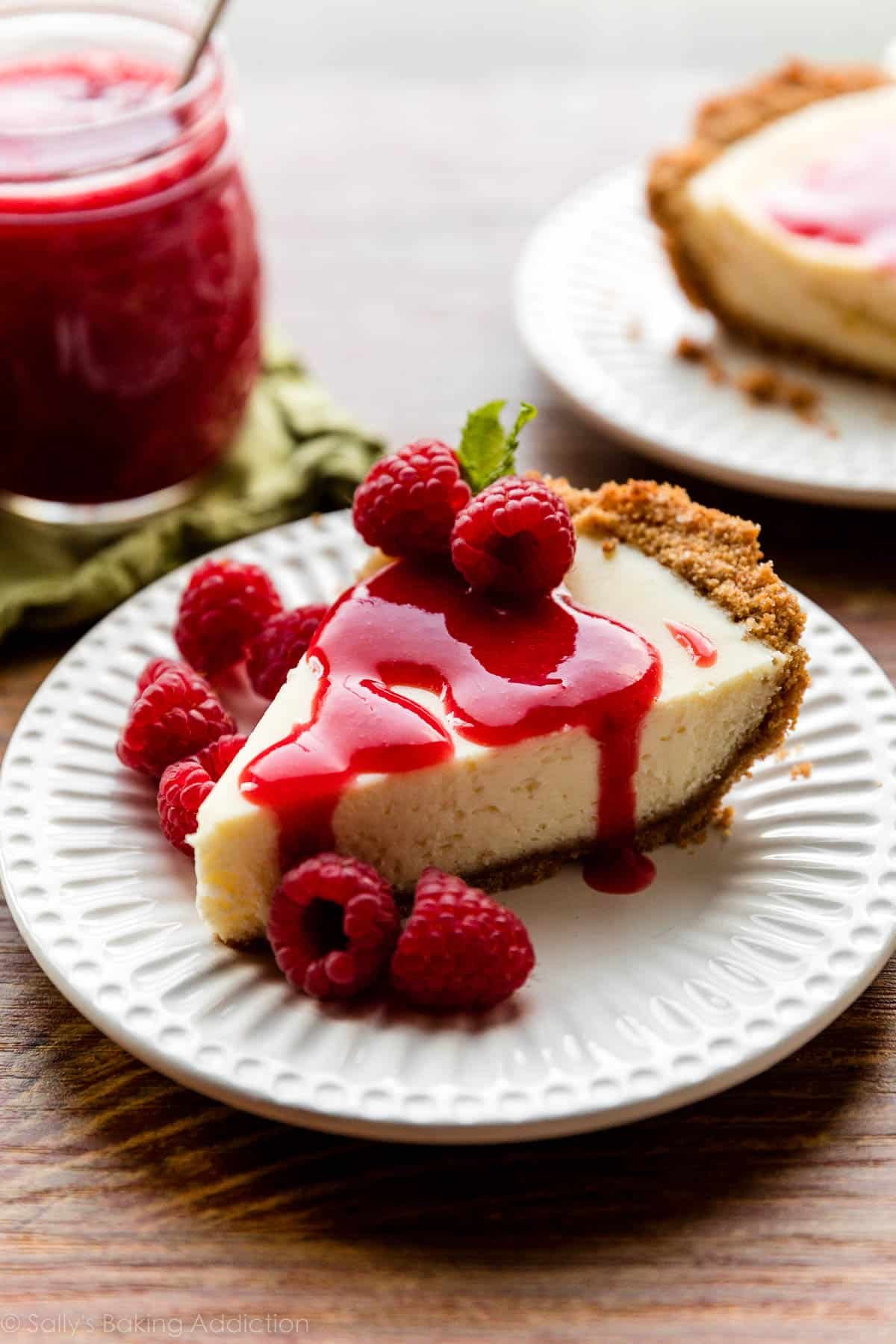 slice of cheesecake on white plate with raspberry sauce and fresh raspberries on top.