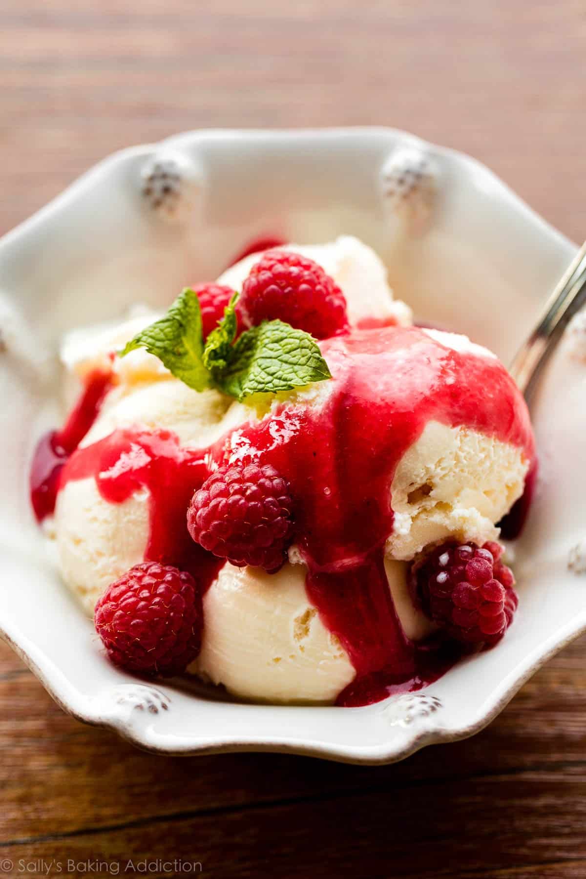 bowl of vanilla ice cream with raspberry sauce and fresh raspberries on top.