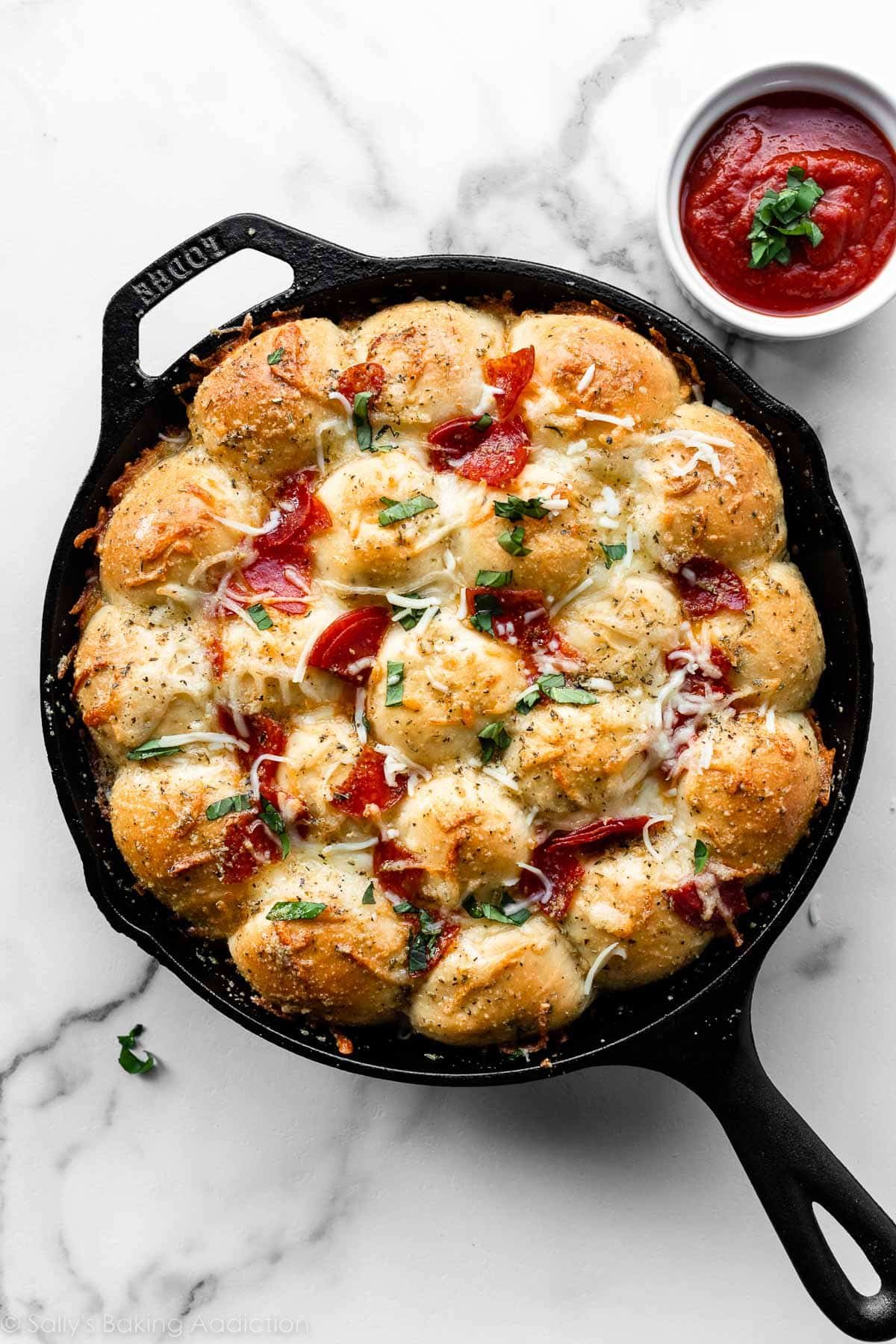 pizza pull apart rolls topped with cheese, pepperoni, and chopped basil in a cast iron skillet.