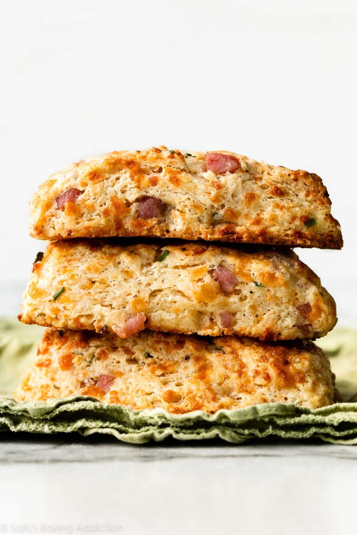 stack of 3 ham and cheddar cheese scones on green linen.