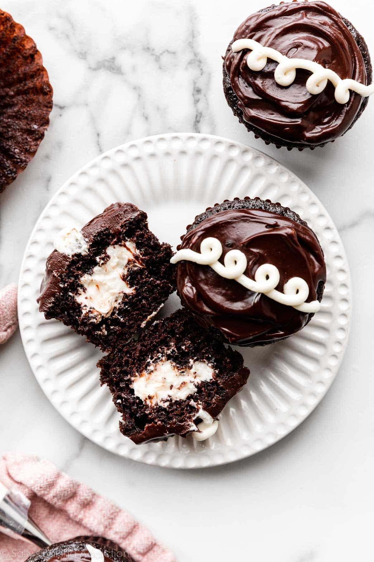 2 Hostess-style homemade cream-filled chocolate cupcakes on white plate.