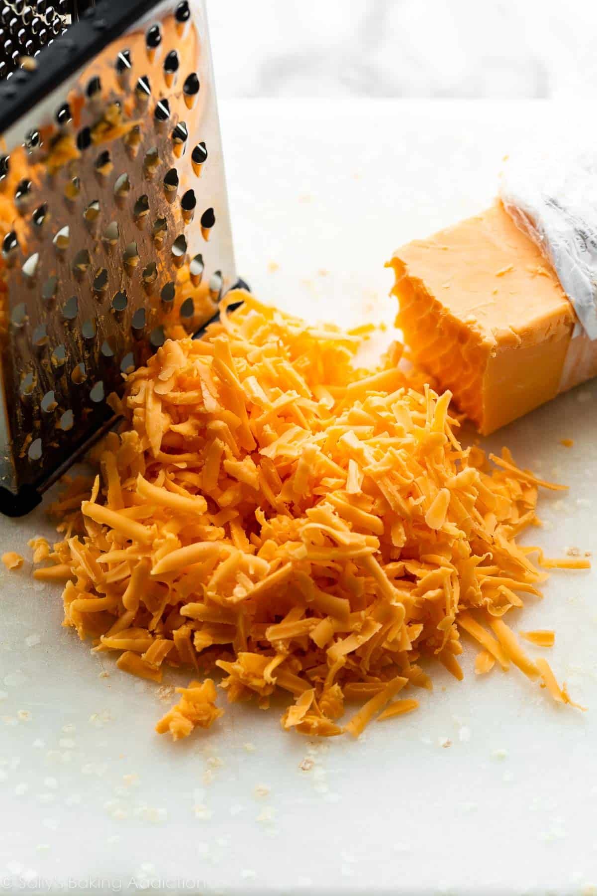 queso cheddar rallado en una tabla de cortar blanca.