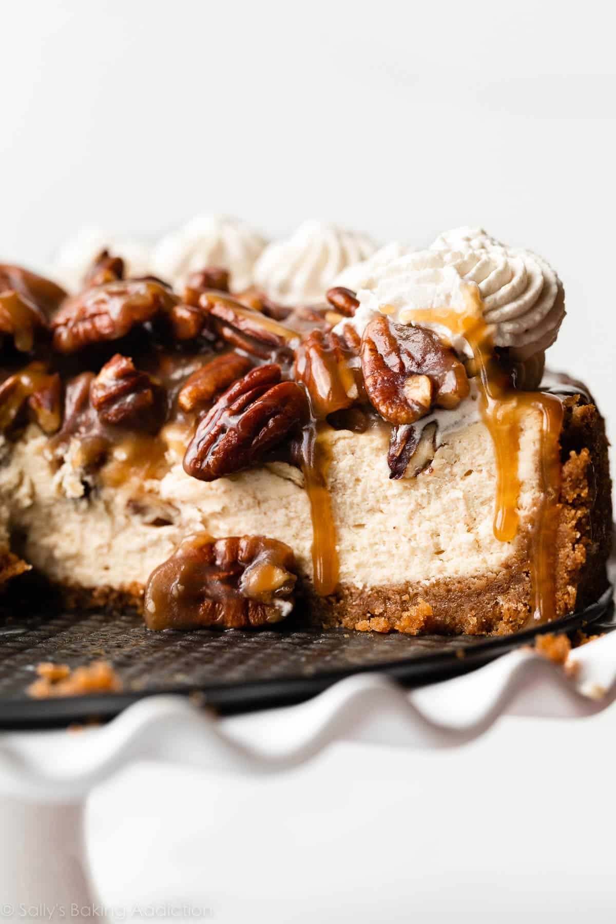 side of a slice of pecan pie cheesecake topped with whipped cream and dripping with caramel.