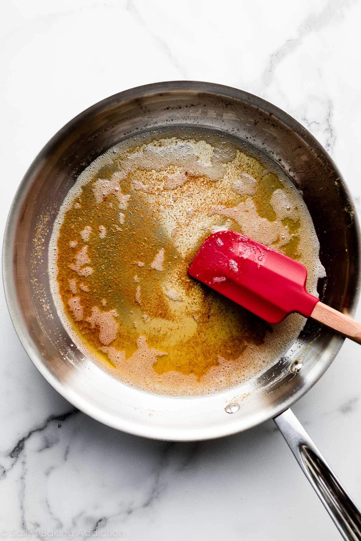 browned butter in metal skillet with red spatula.