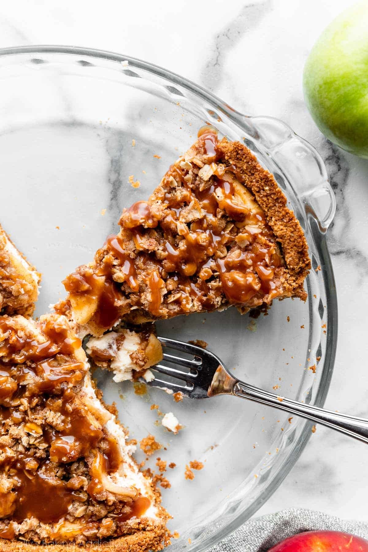 cut slice of caramel apple cheesecake pie in glass pie dish with fork sitting next to it.