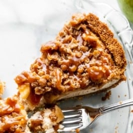 up close slice of caramel apple pie cheesecake sitting in glass pie dish.