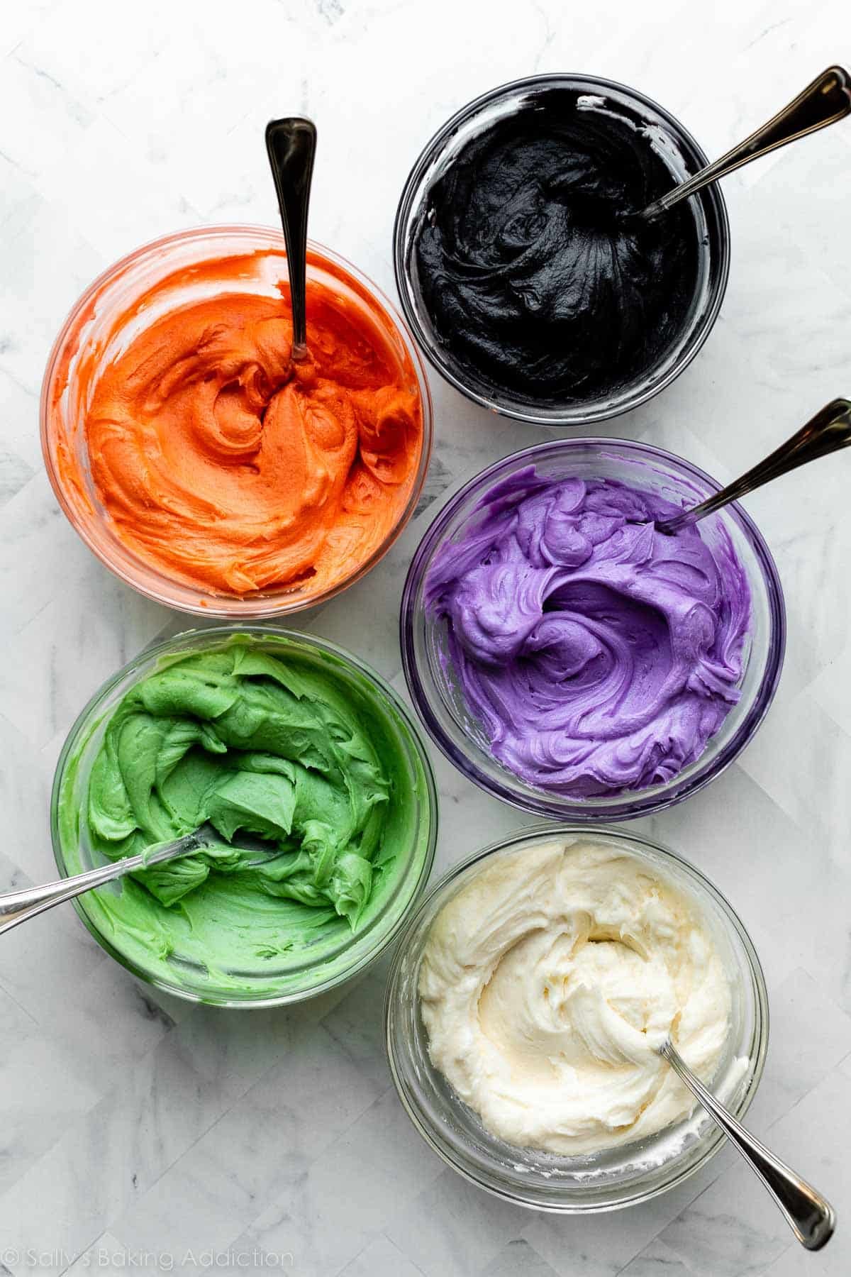 green, white, purple, orange, and black frostings in separate glass bowls.