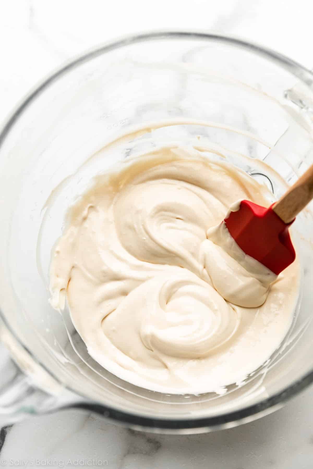 cheesecake batter in glass mixing bowl with red spatula.