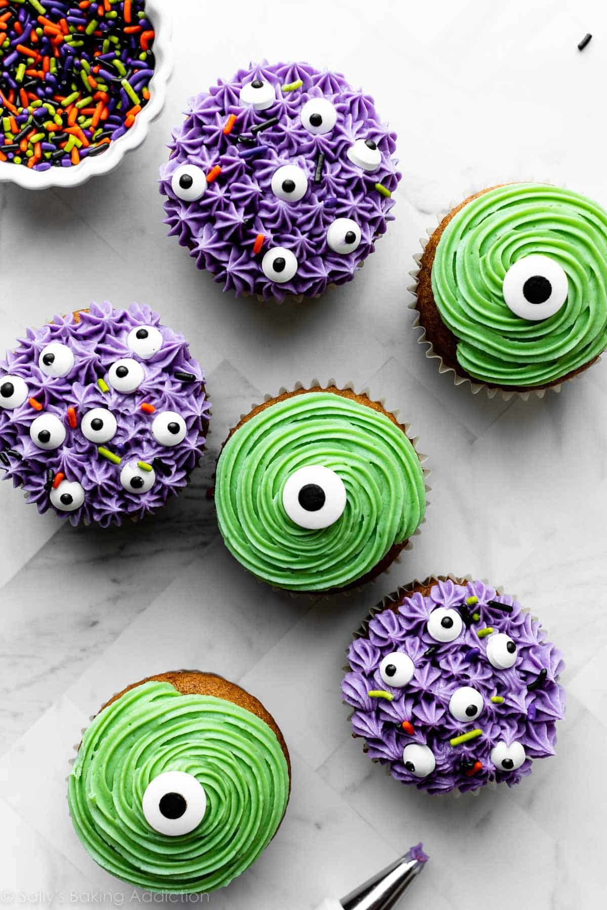 cupcakes decorated as monsters with green frosting and purple frosting, plus candy eyeballs and Halloween sprinkles.