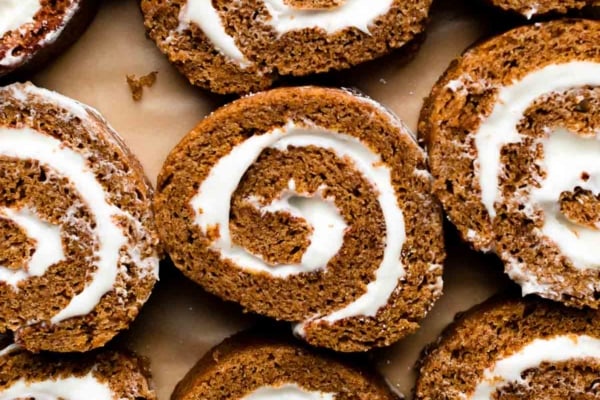 slices of pumpkin roll filled with cream cheese frosting arranged on brown parchment paper sheet.