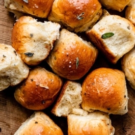 dinner rolls garnished with fresh chopped sage on wooden cutting board.