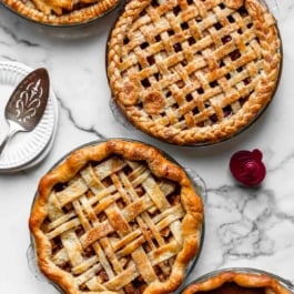 4 baked pies with different pie crust designs on marble counter.