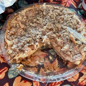 Photo of caramel apple cheesecake pie with a couple sliced removed.