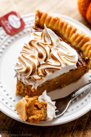 slice of pumpkin pie with toasted meringue topping on white plate with forkful also on plate.
