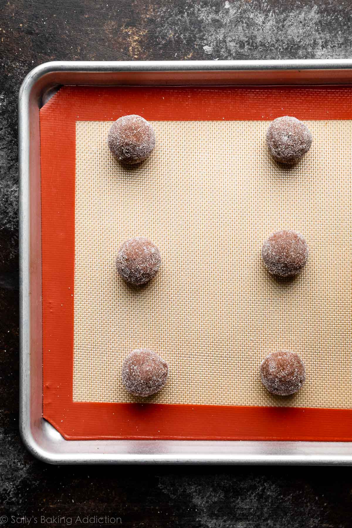 6 cookie dough balls arranged on silicone baking mat-lined baking sheet.
