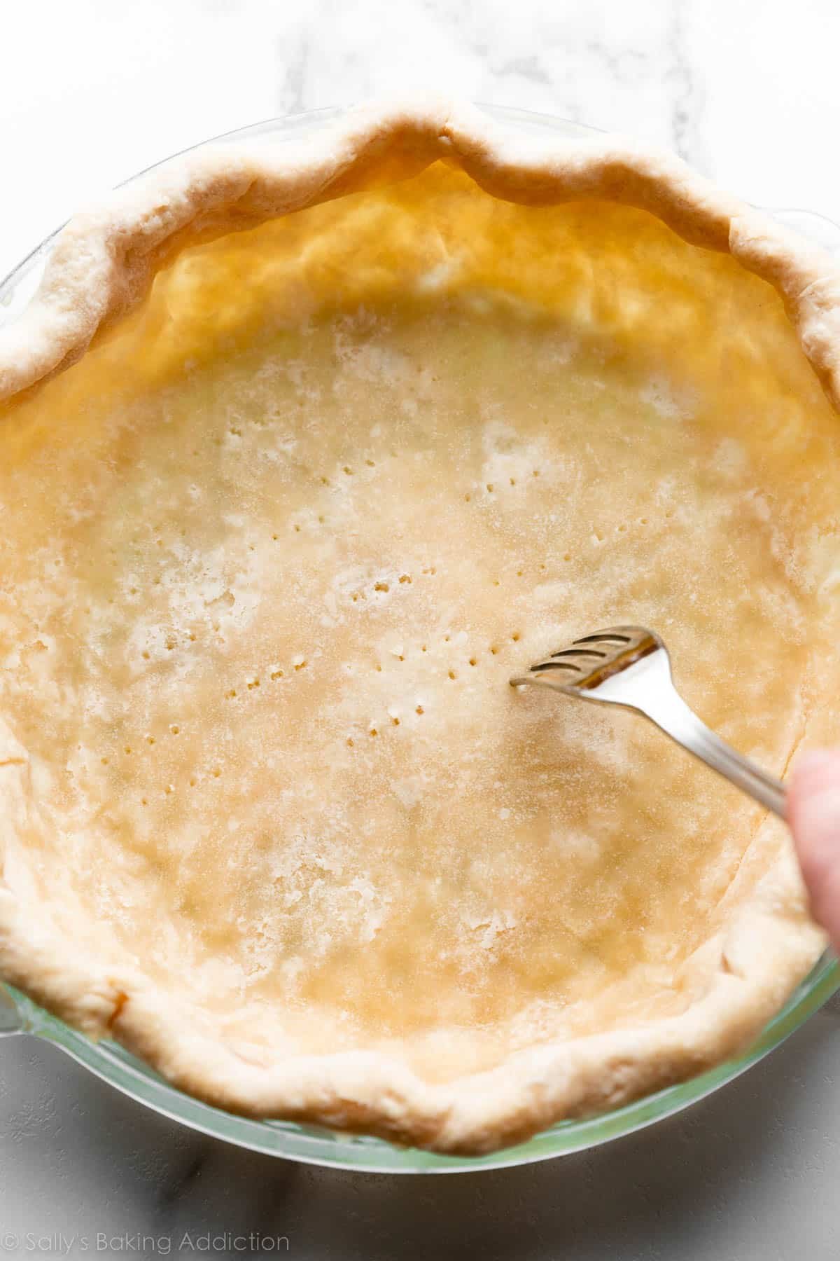 pricking the bottom of par-baked pie crust with fork.