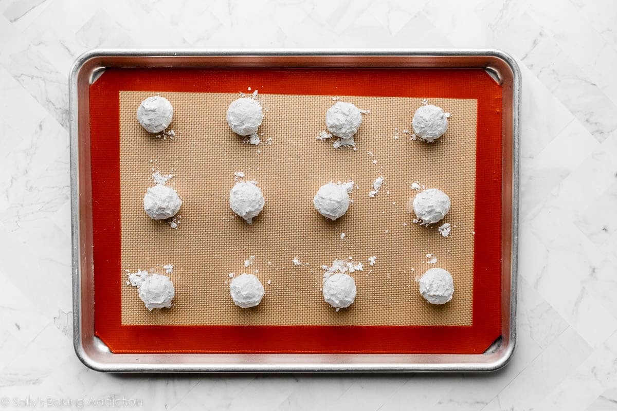confectioners' sugar coated dough balls on lined baking sheet.