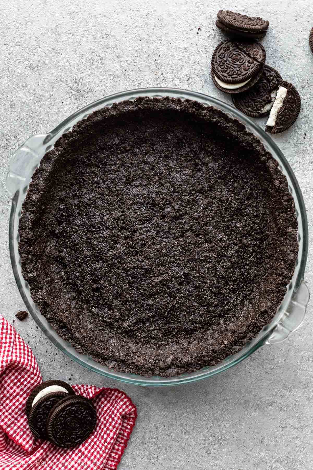 Oreo cookie crust pressed in glass pie dish on gray backdrop.