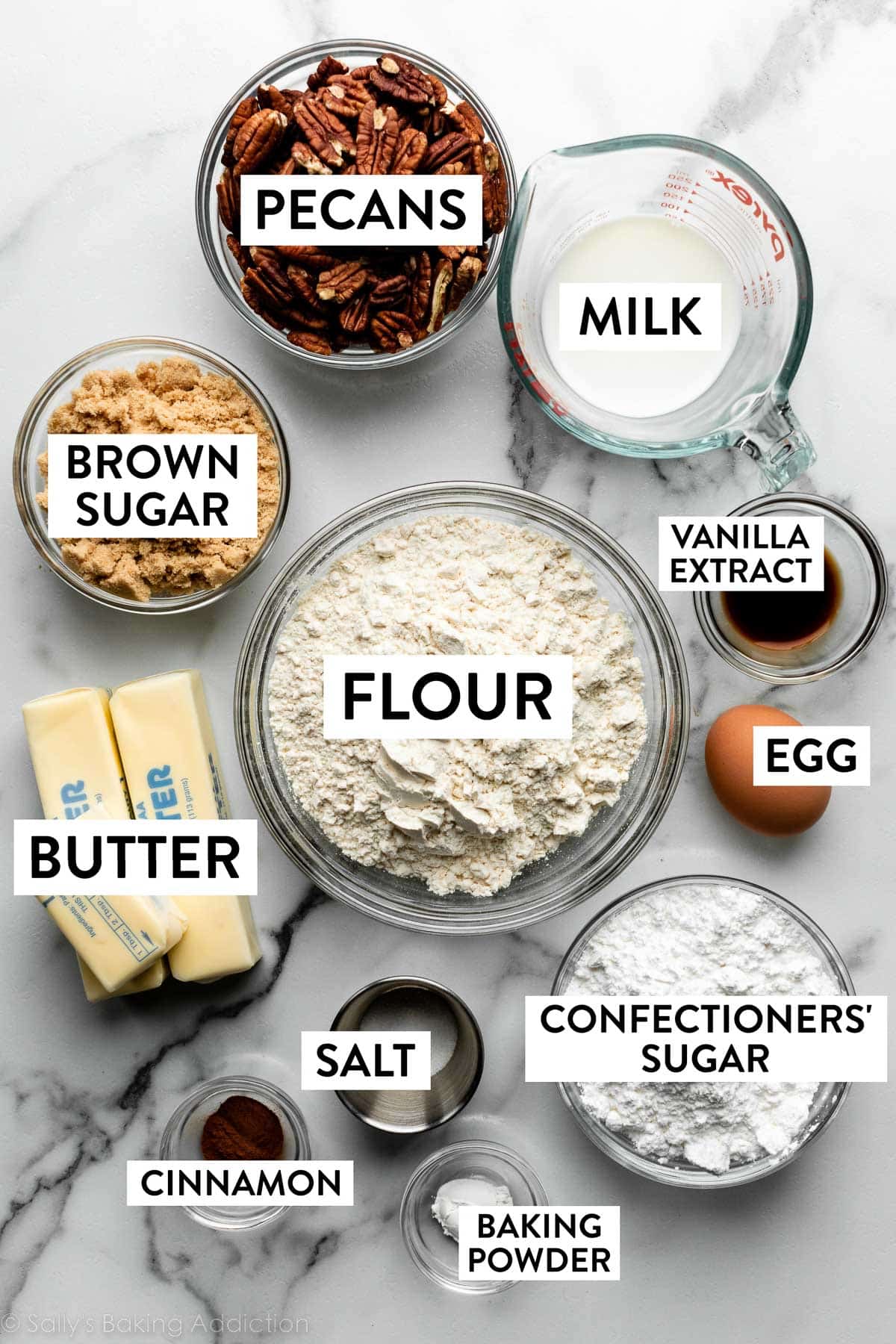 ingredients measured and displayed on marble counter including flour, milk, butter, egg, baking powder, cinnamon, pecans, and brown sugar.