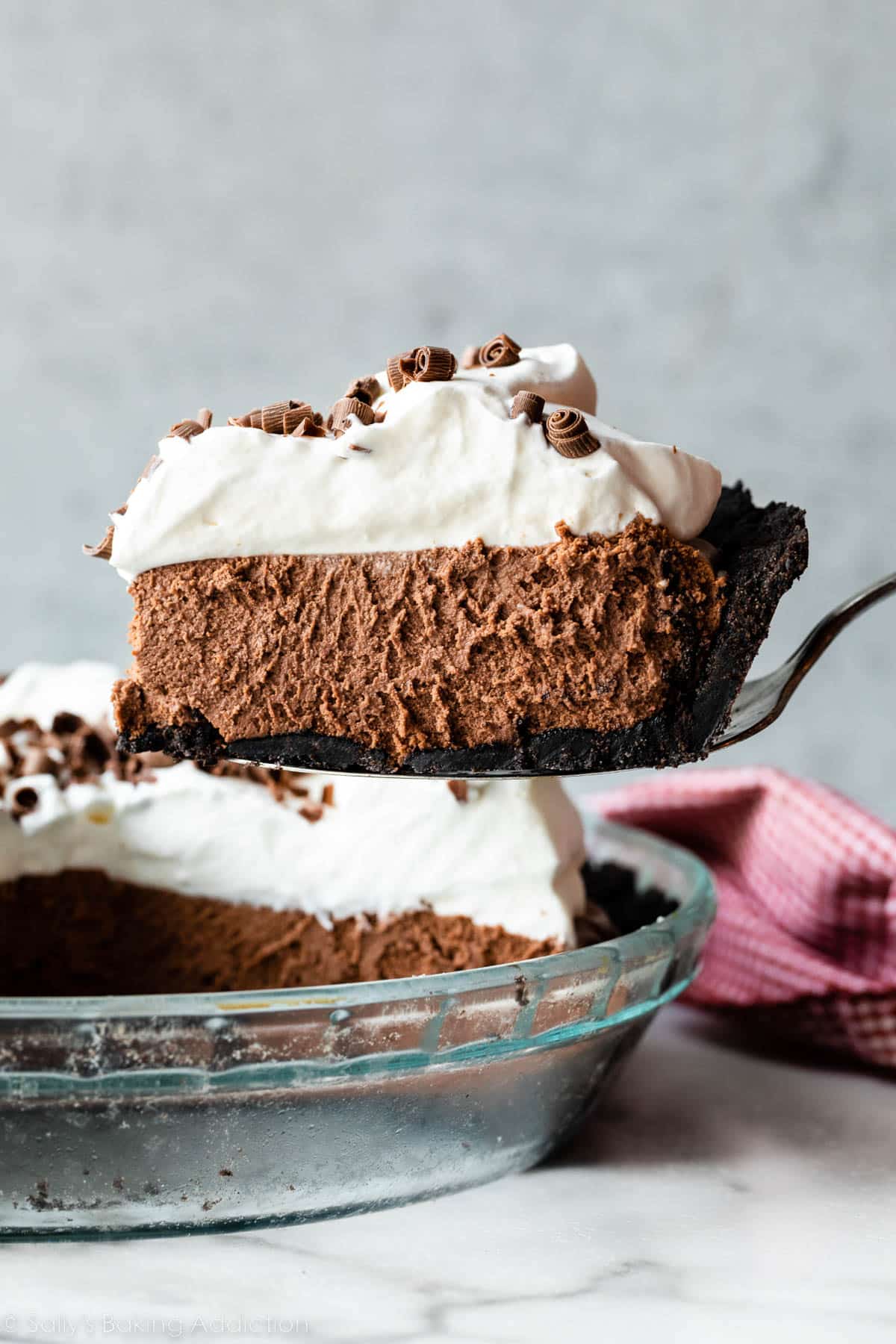 slice of chocolate French silk pie on Oreo cookie crust with whipped cream and chocolate curls on top.