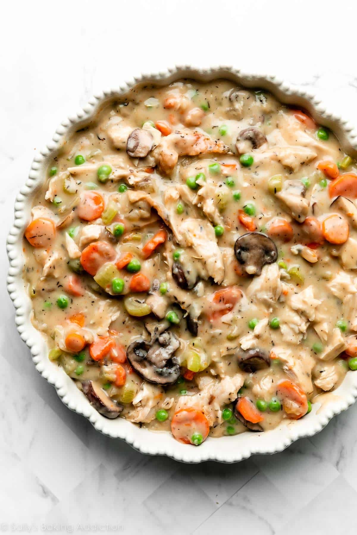 turkey pot pie filling with gravy, carrots, peas, and mushrooms in pie dish.