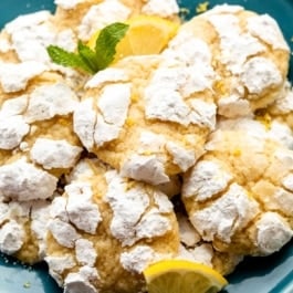 lemon crinkle cookies arranged on blue plate with lemon slices and fresh mint.