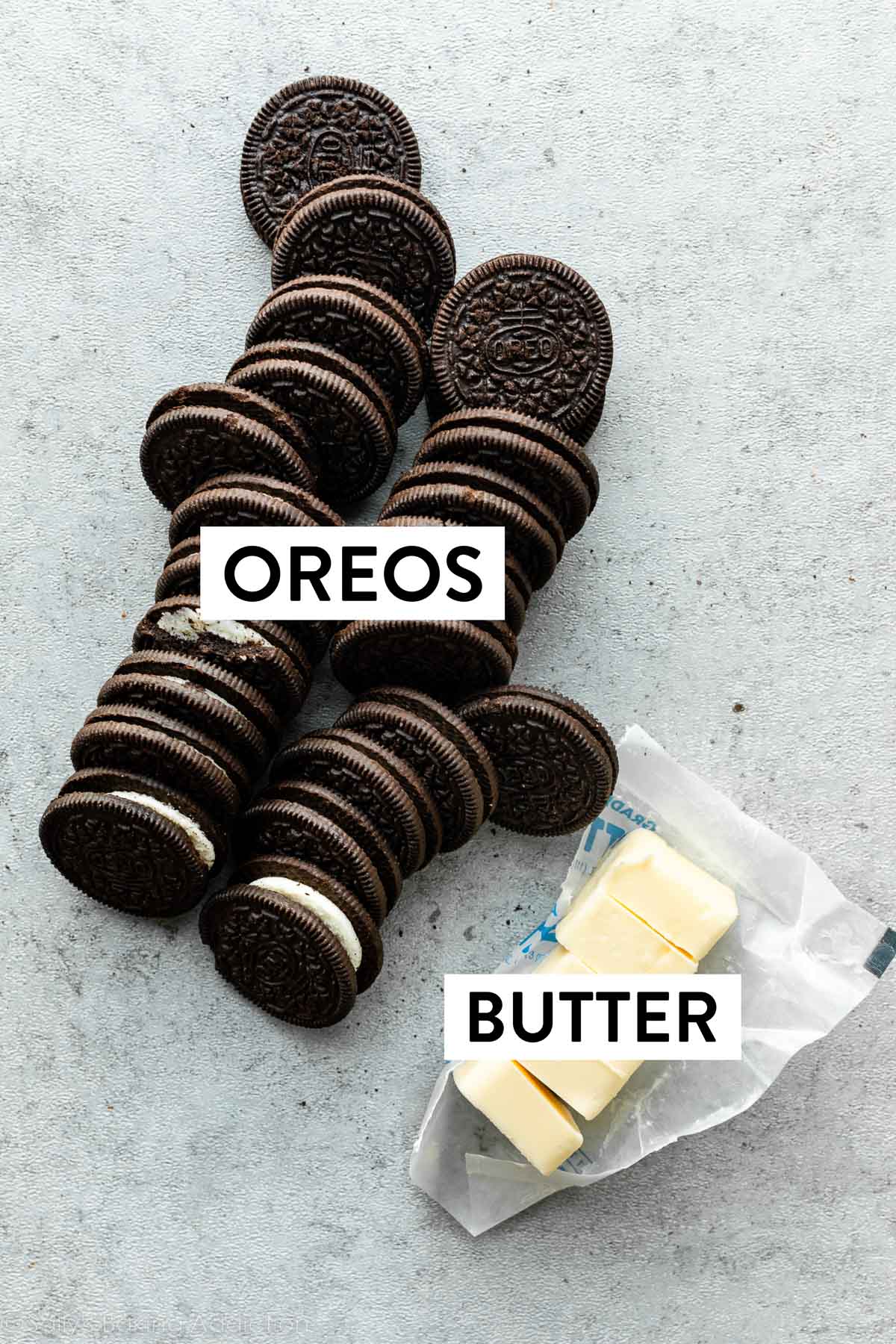 Oreo cookies lined up and butter sliced into 5 pieces on gray backdrop.