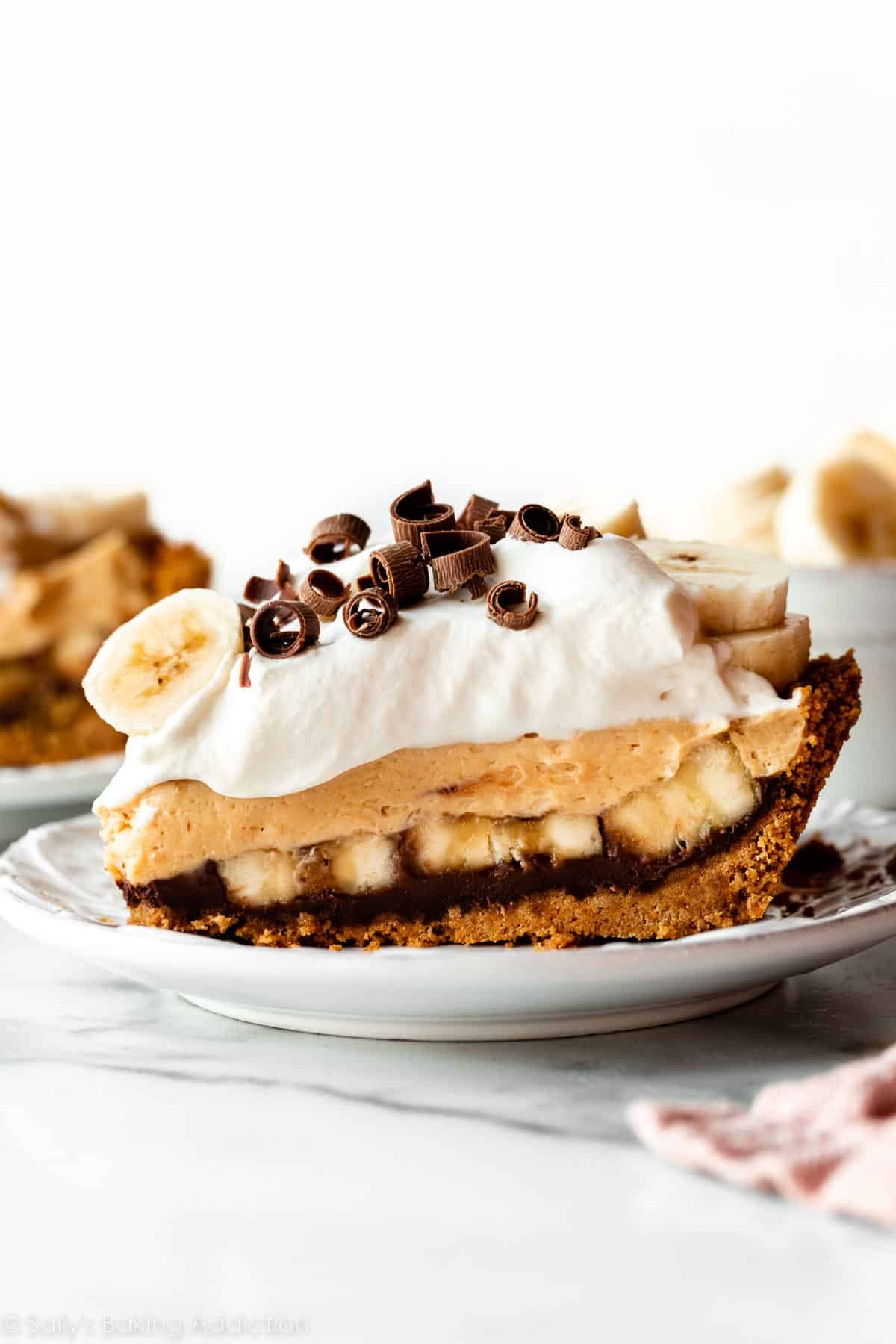 slice of pie on plate with layers of chocolate ganache, bananas, peanut butter, and whipped cream with chocolate curls.