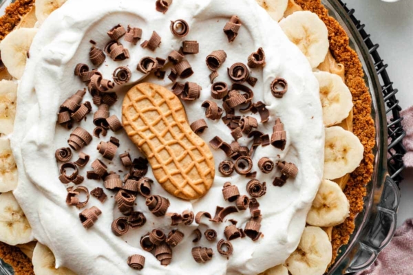 peanut butter banana cream pie with whipped cream, chocolate curls, and Nutter Butter cookie on top.