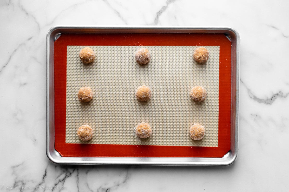 9 peanut butter cookie dough balls on silicone baking mat-lined baking sheet.