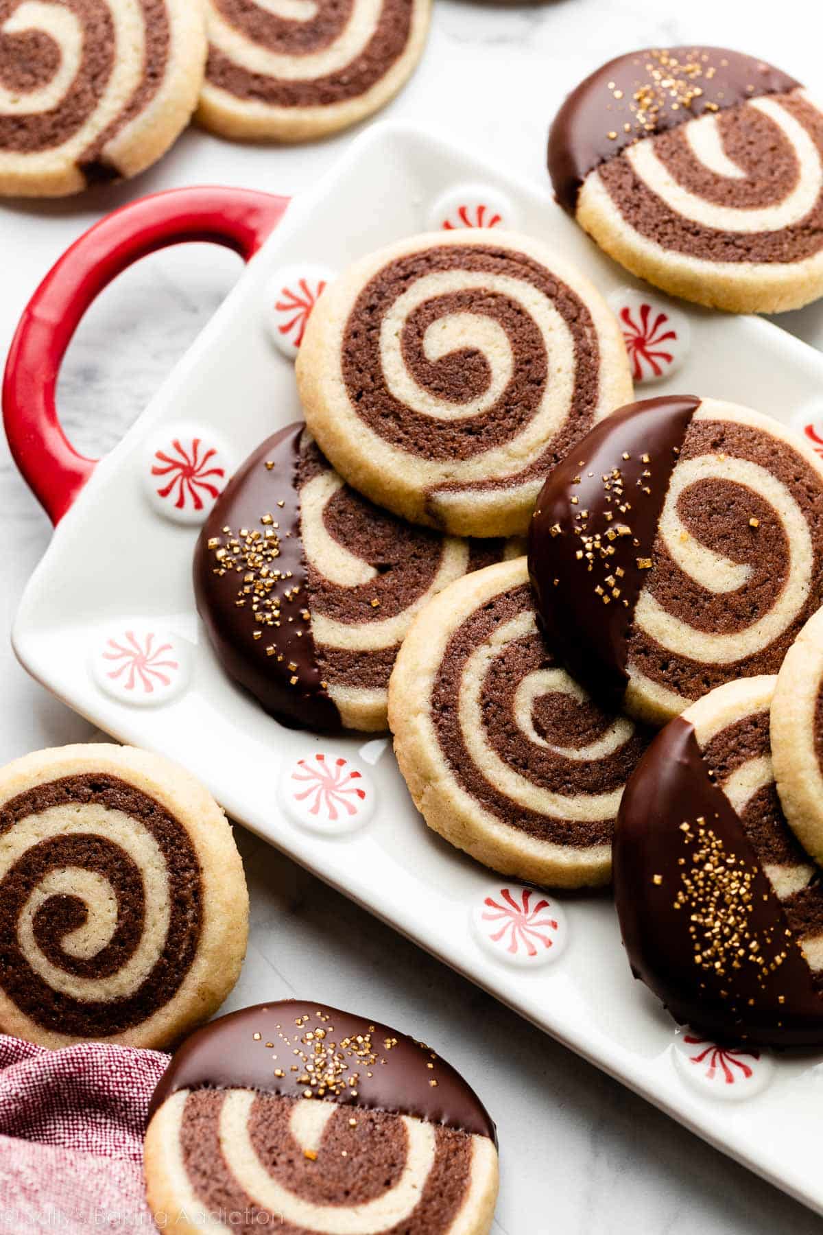 pinwheel cookies arranged on white plate with peppermint swirls around the edges.