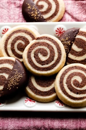 pinwheel cookies on white plate with peppermint swirls sitting on red linen.