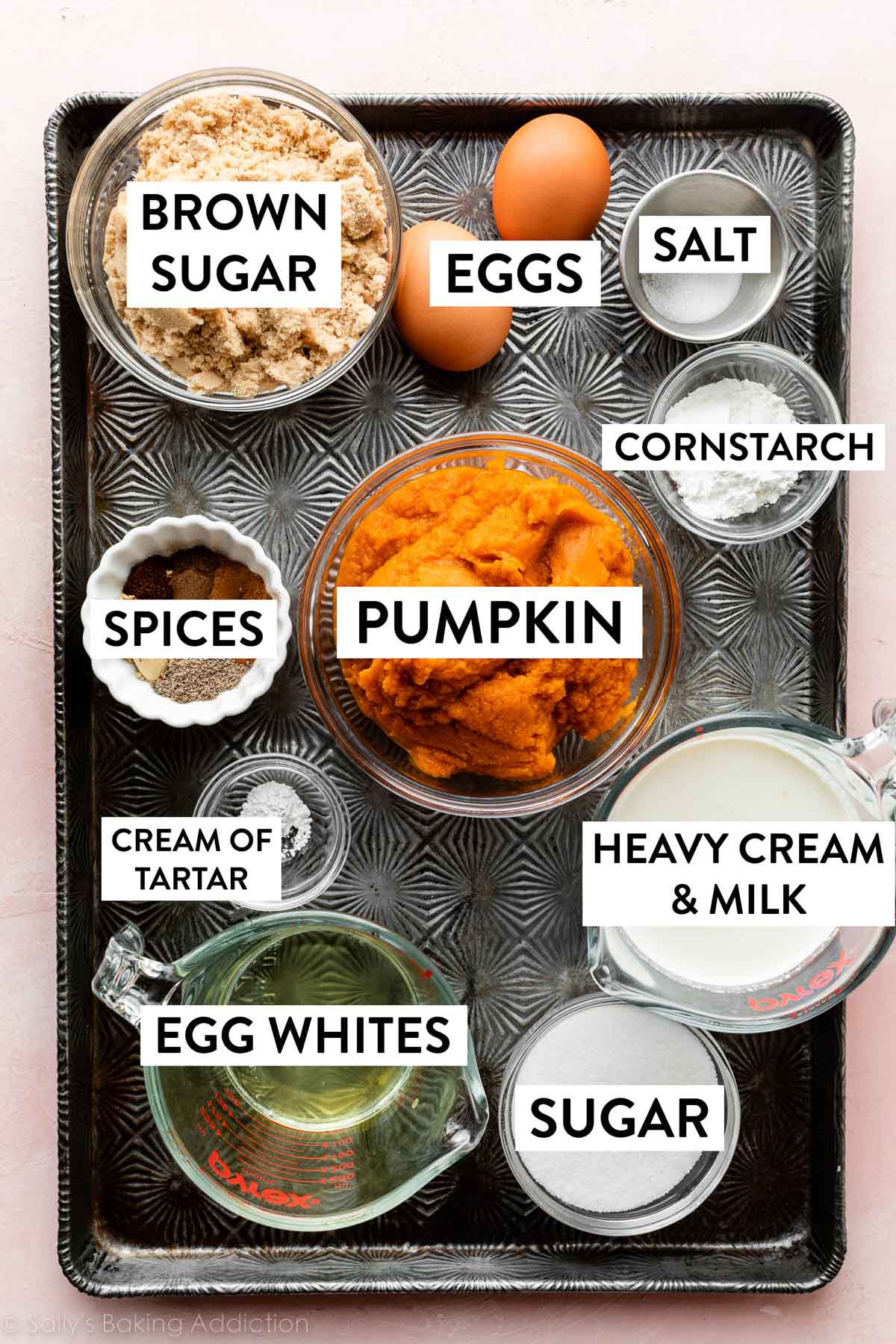 ingredients on baking sheet including pumpkin, heavy cream, milk, brown sugar, eggs, and spices.