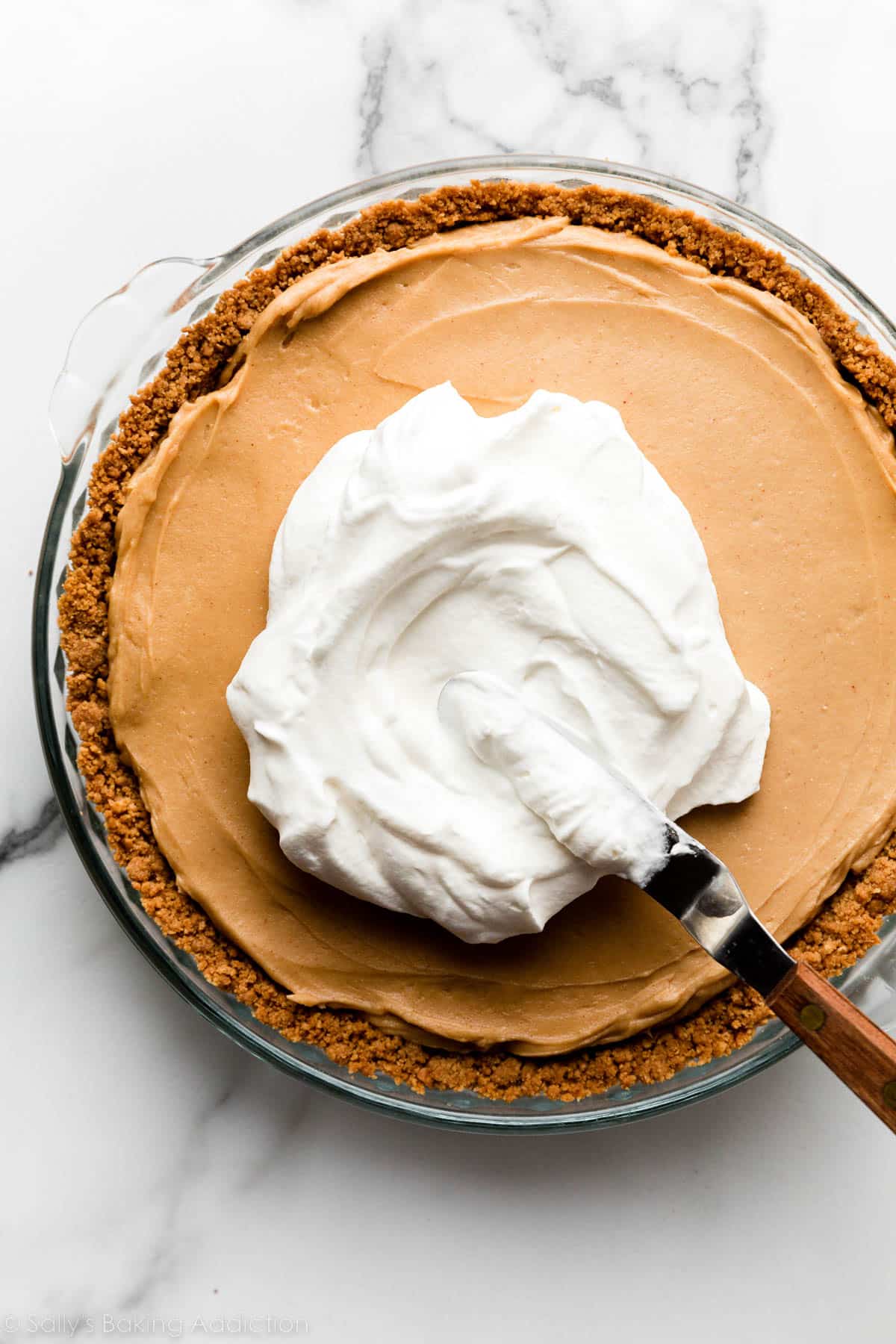 spreading whipped cream on peanut butter pie with peanut butter cookie crust.