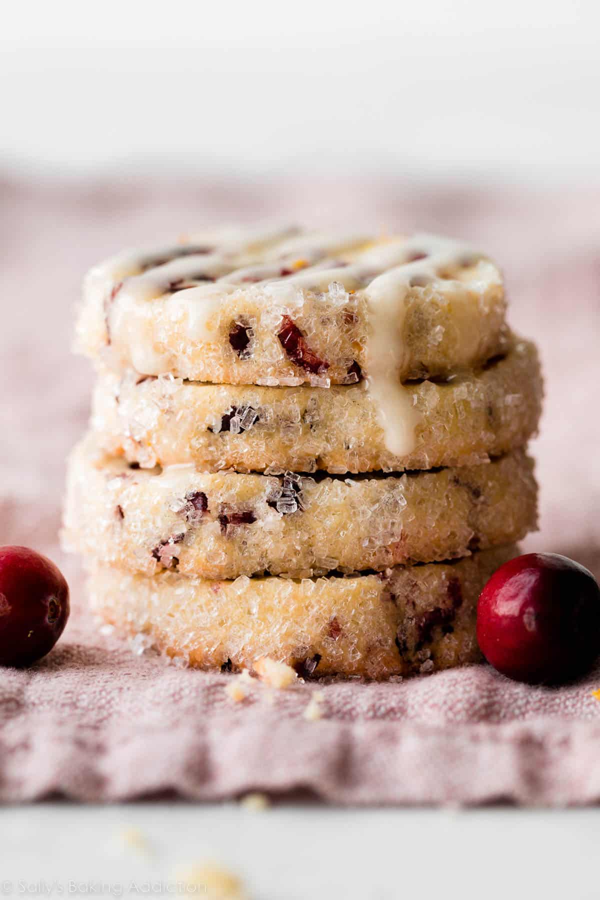 stack of cranberry cookies rolled in coarse sugar sprinkles with the top one covered in icing.