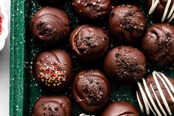 chocolate covered oreo balls truffles topped with crushed Oreo cookie crumbs and arranged on green baking sheet.