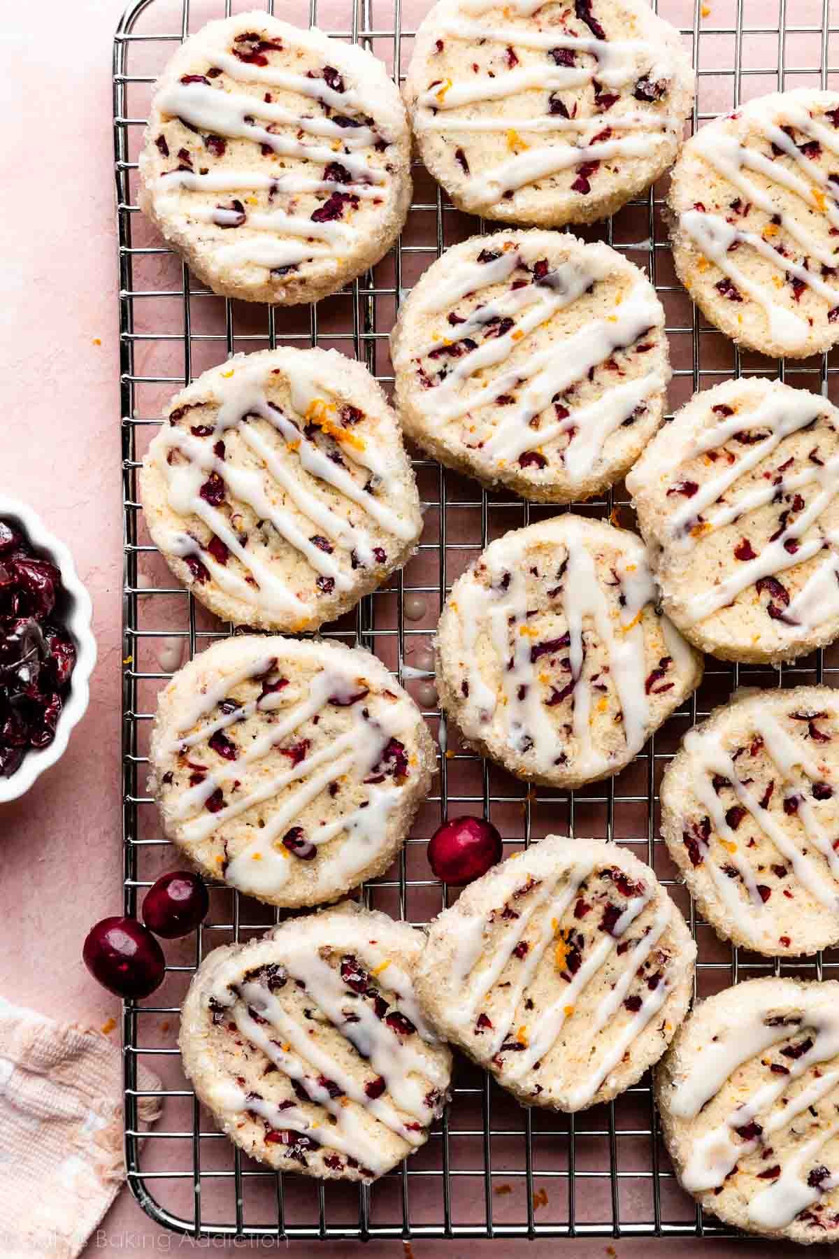 cranberry orange cookies with dried cranberries and orange icing drizzled on top arranged on cooling rack.