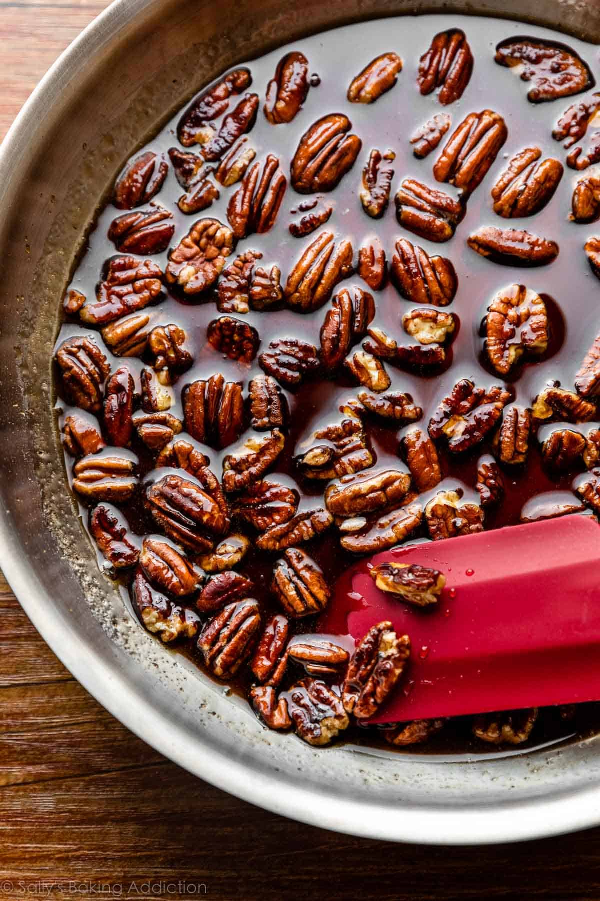 skillet of maple syrup pecans with red spatula.