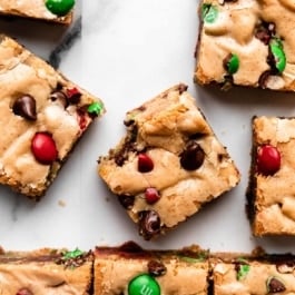 M&M cookie bar squares on white parchment paper with center bar with bite taken out.