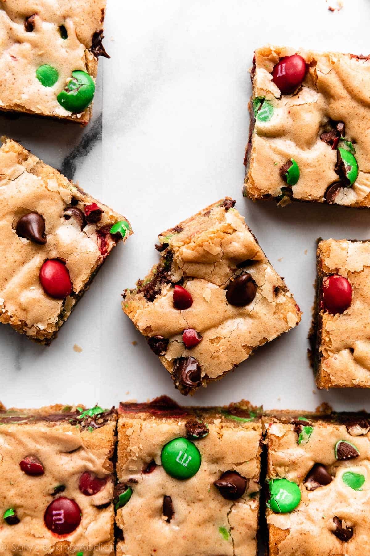 M&M cookie bar squares on white parchment paper with center bar with bite taken out.