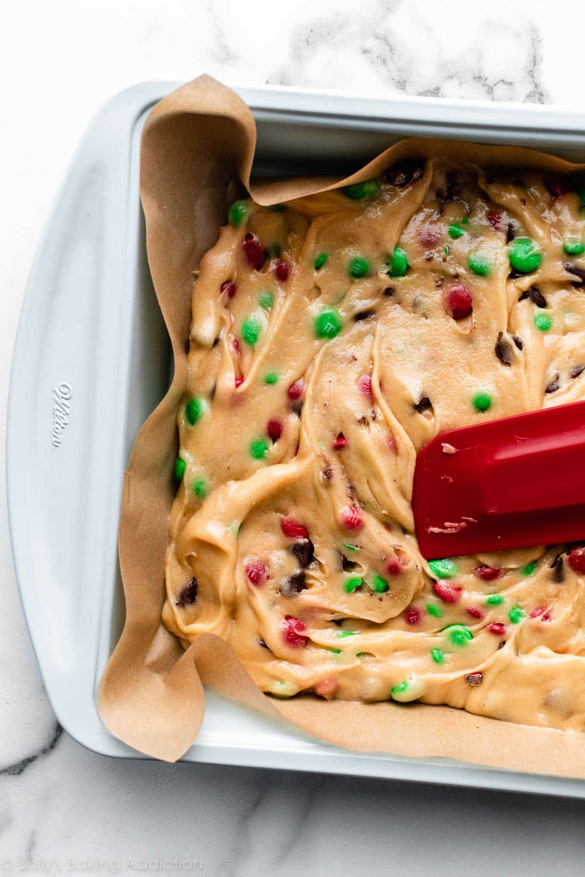 cookie dough with M&Ms spread in parchment paper-lined blue baking pan.
