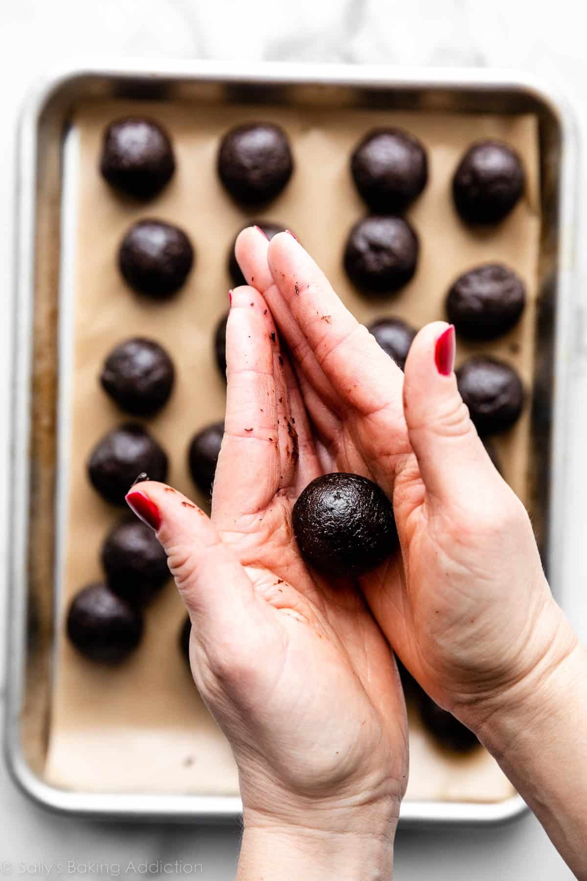 two hands rolling an Oreo cookie ball over a tray of rolled Oreo balls.