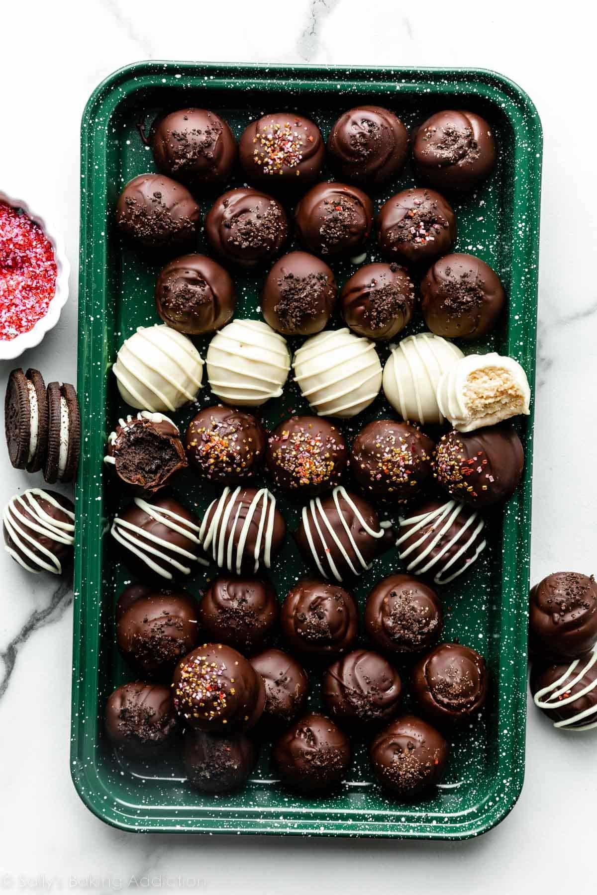 chocolate coated and white chocolate coated and drizzled oreo truffle balls on green baking sheet.